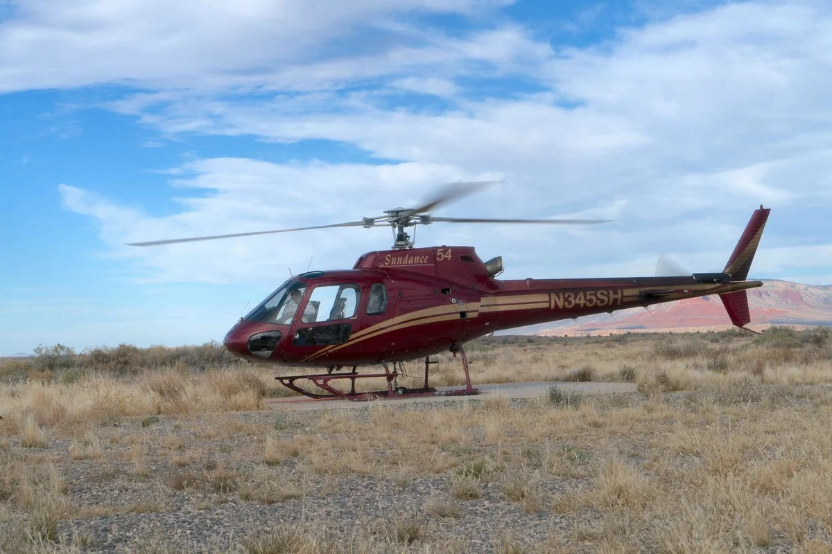 Red Sundance helicopter, tail number N345SH, on a desert landing pad with red rock cliffs behind